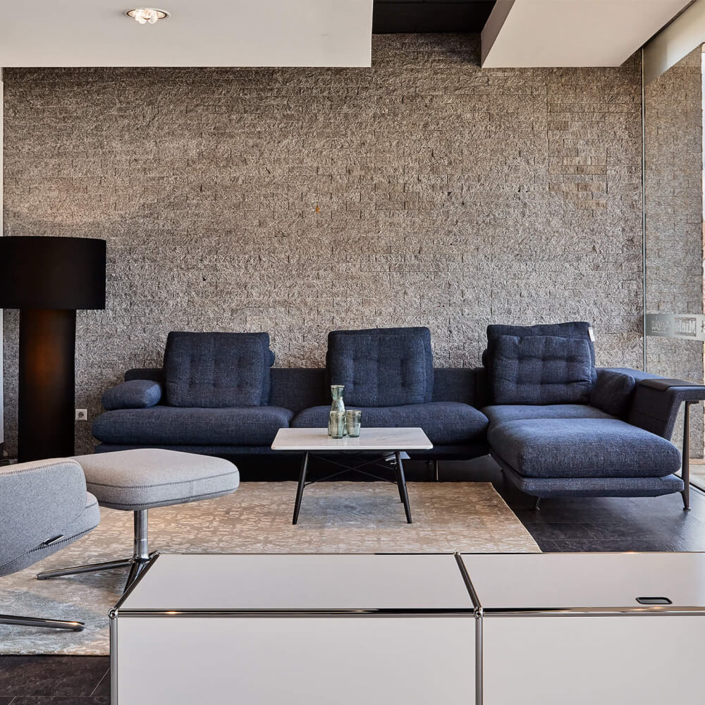 blaue Sitzecke mit Beistelltisch, grauer Sessel mit Fußablage - Wohnen, Wohnzimmer, Sofa, Wohnlandschaft, Beistelltisch, Wohnzimmertisch, Teppich, Accessoires - bühler einrichtungen in Friesenheim bei Offenburg zwischen Karlsruhe und Freiburg