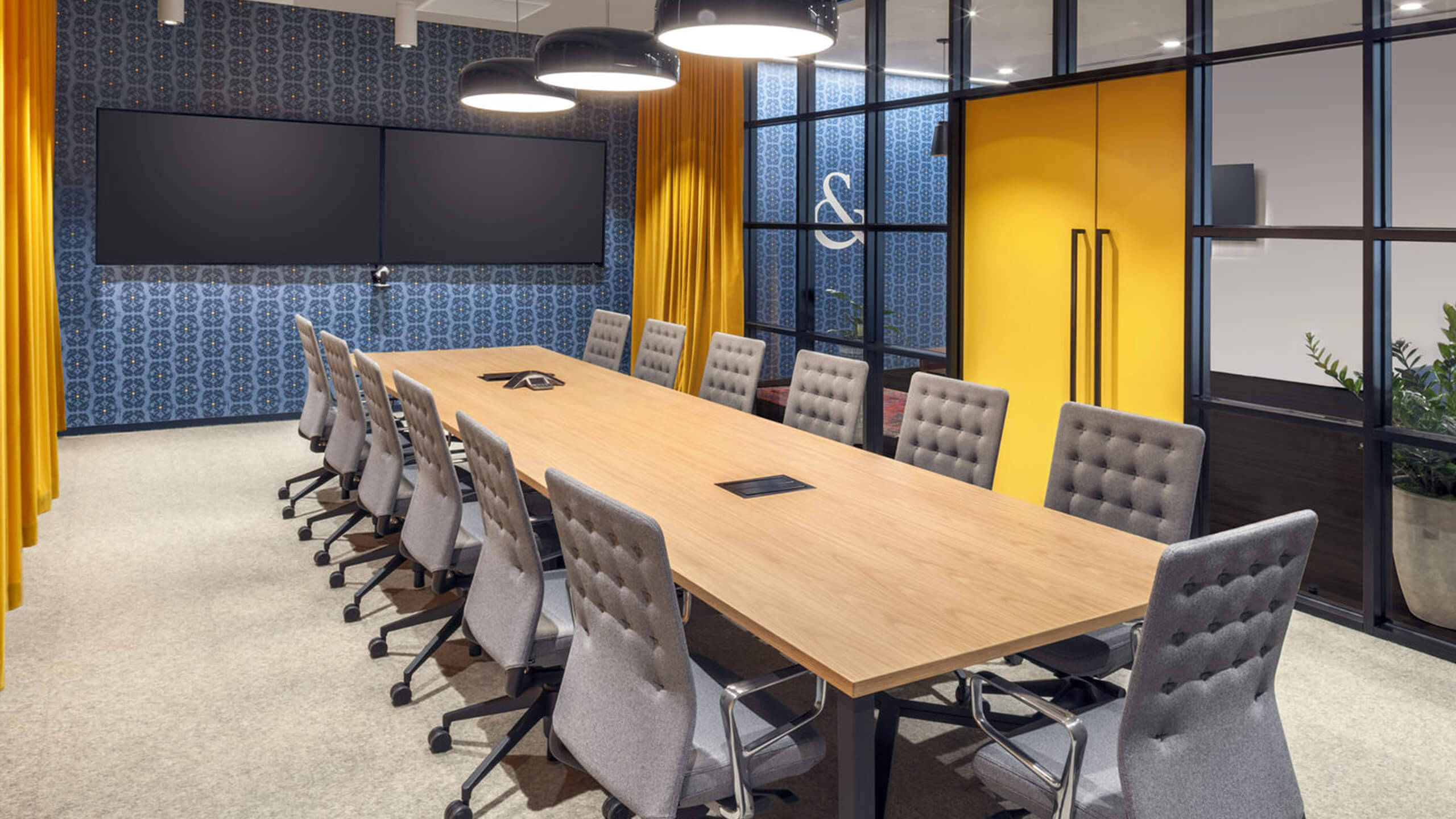 Konferenzraum mit hellem Holztisch, grauen Stühlen und gelben Gardinen